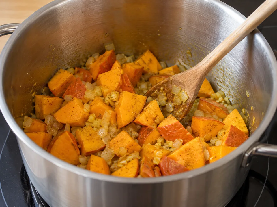 Kürbiswürfel mit Schale zu Zwiebel und Ingwer geben und mit dem Curry kurz anschwitzen.